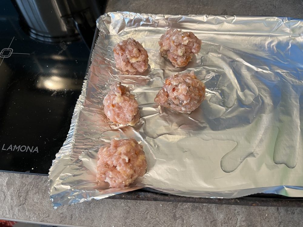 Five raw meatballs on a foiled baking tray.
